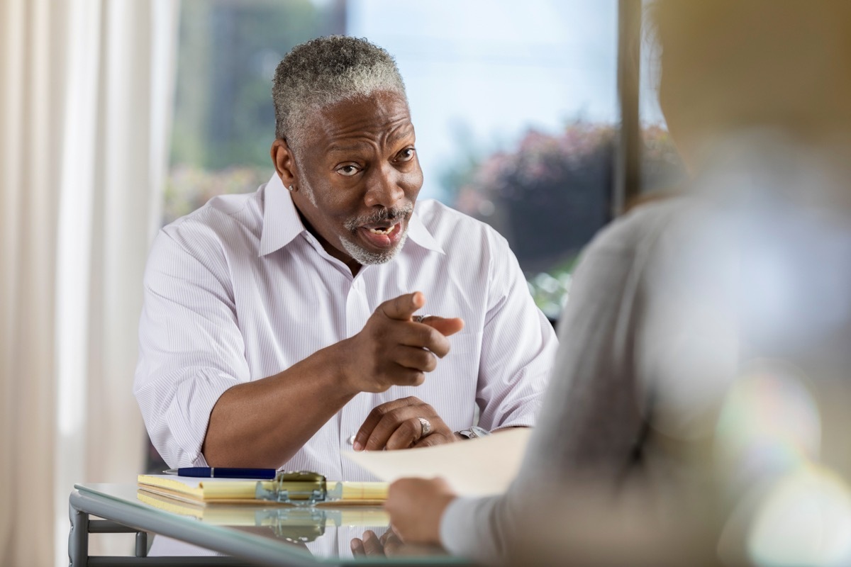 serious senior male office manager points to a female employee while reprimanding her.