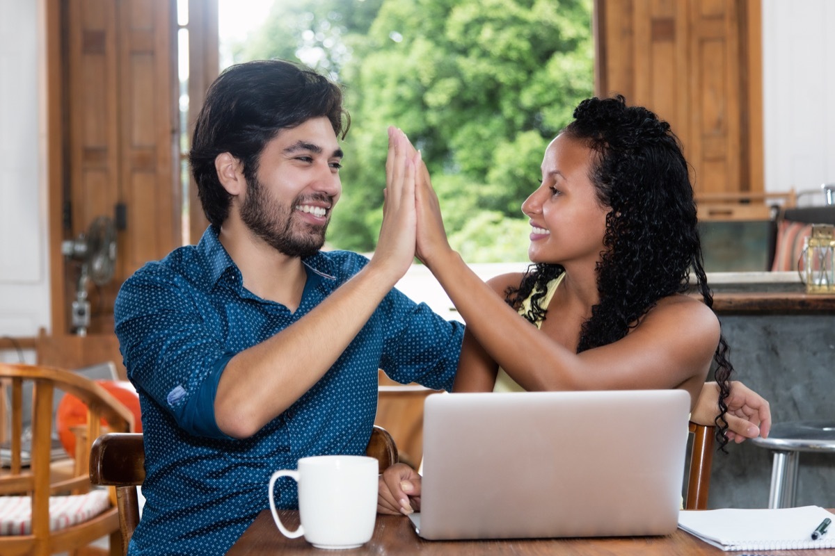 Multicultural couple high-fiving using computer