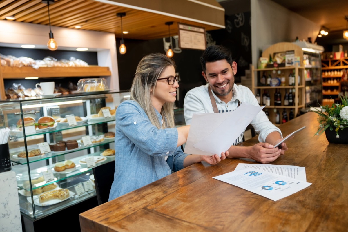 white woman at bakery showing a paper to younger latino employee