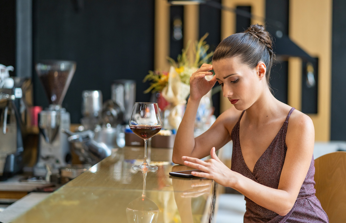 Sad woman sitting at a bar being stood up and using smart phone