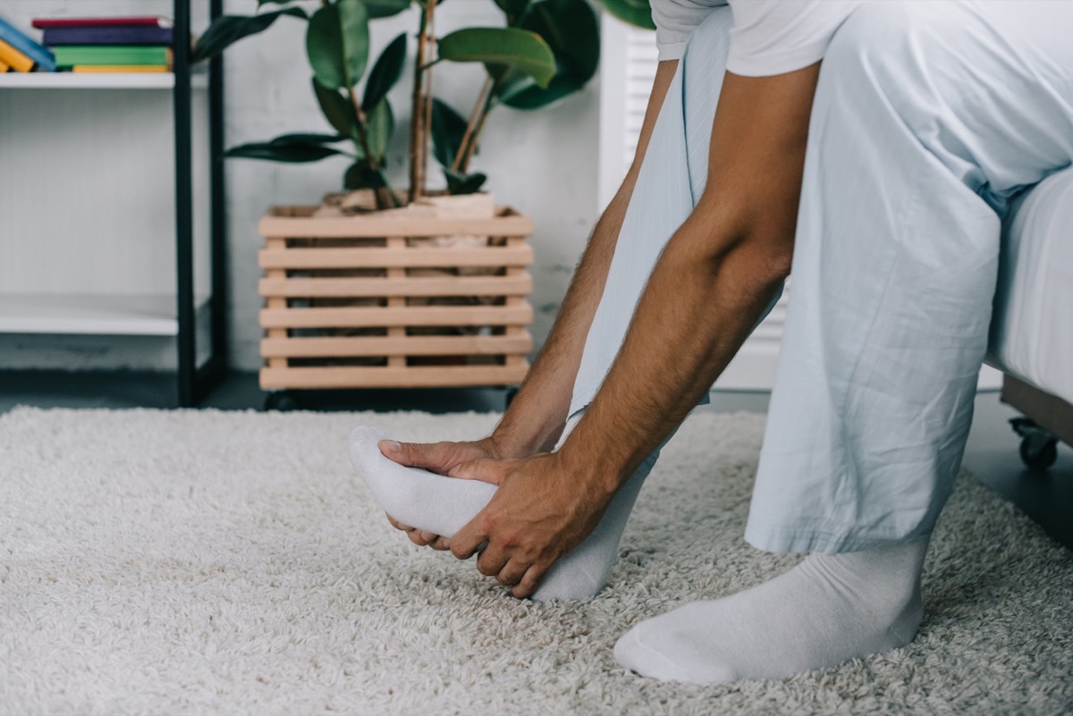 cropped shot of man sitting on bed and suffering from foot pain