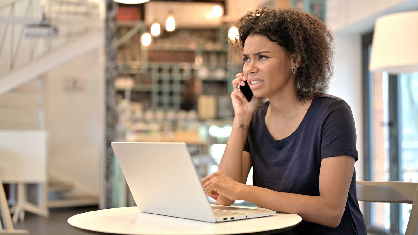 A young woman sitting in a cafe while answering a phone call with a confused look on her face