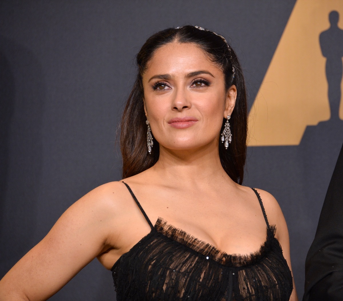 salma hayek wearing a black dress and long earrings on a red carpet