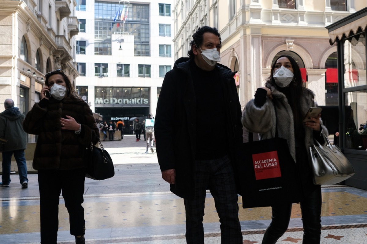 people walking on street in italy wearing masks to prevent coronavirus