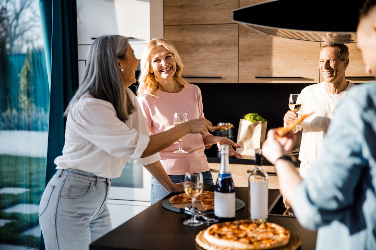 Cheerful men and women drinking wine and chatting in the kitchen