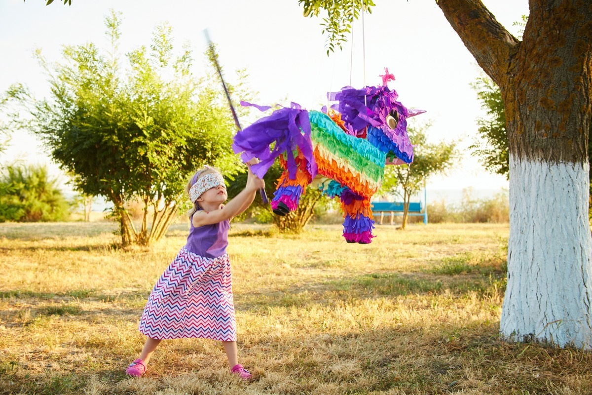 girl with blindfold hitting a multicolored piñata