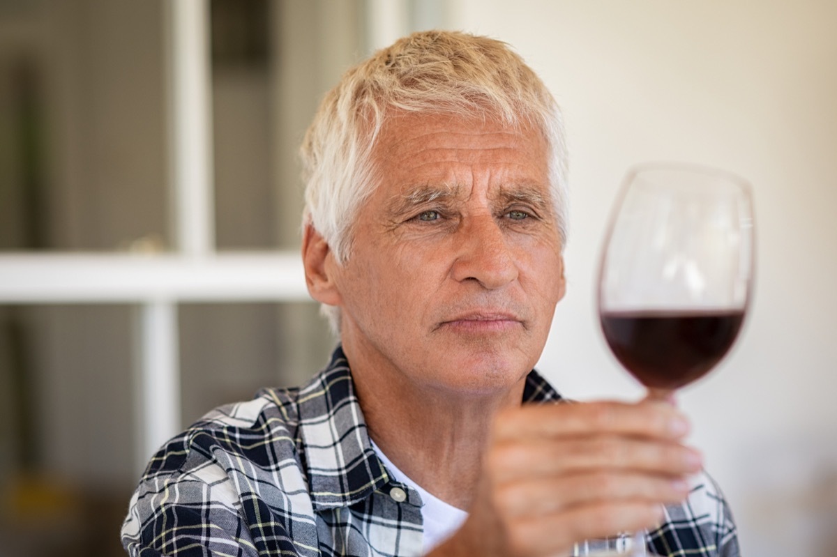 Senior man holding and looking through a glass of red wine.