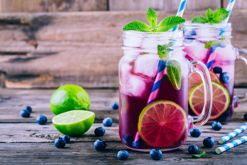 Blueberry ice mojito with lime and mint in mason jar on wooden background