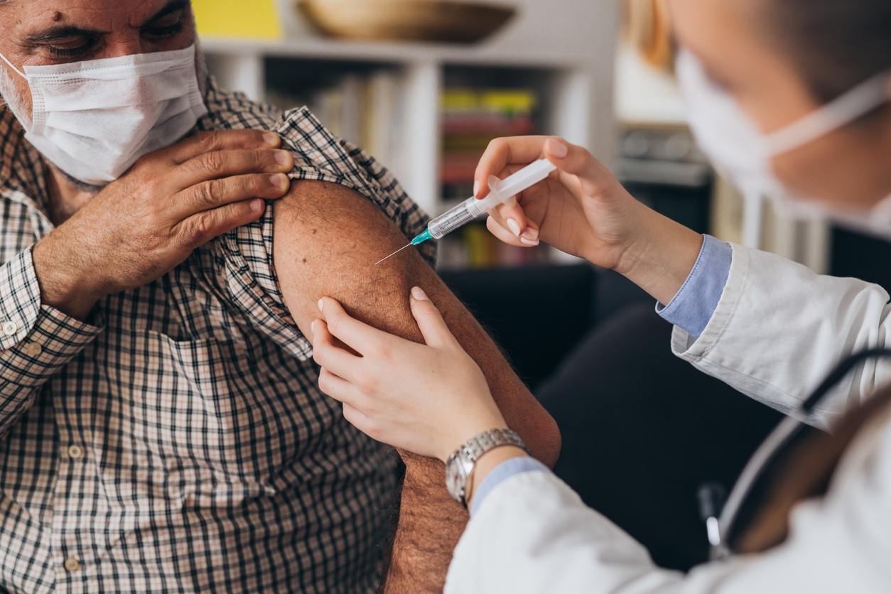 A senior man receives a COVID-19 vaccine injection in his arm from a healthcare worker.