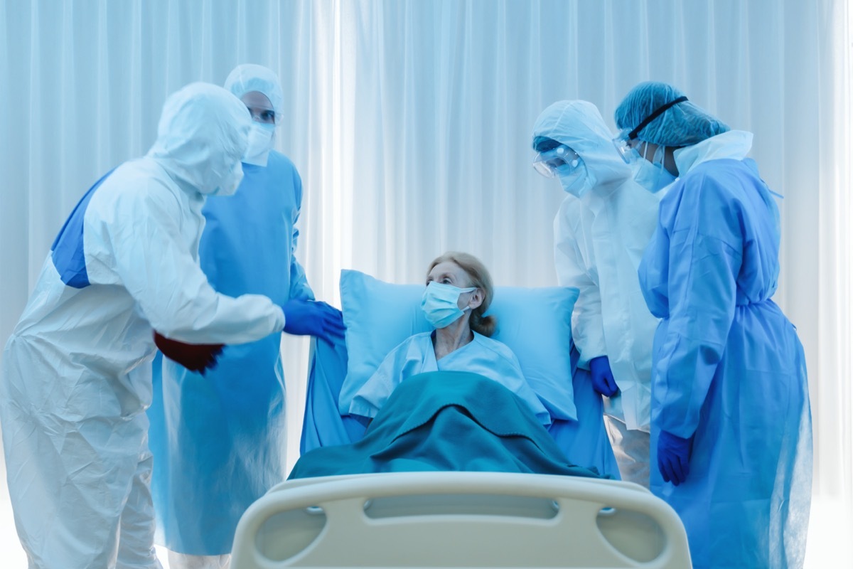 senior coronavirus covid-19 infected patient lying on bed in quarantine room of hospital with doctor and medical staffs aking her symptoms of coronavirus covid-19 sickness for treatment