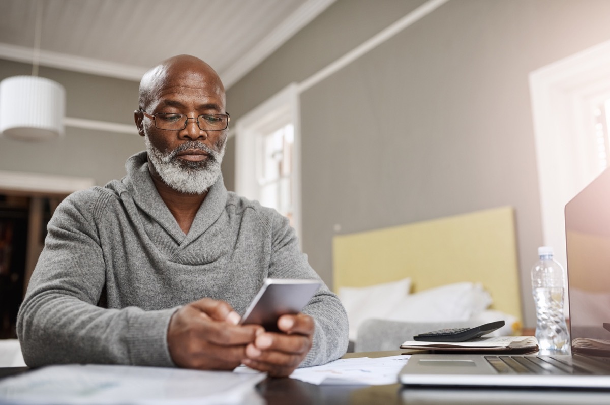 older black man checking his phone at his desk