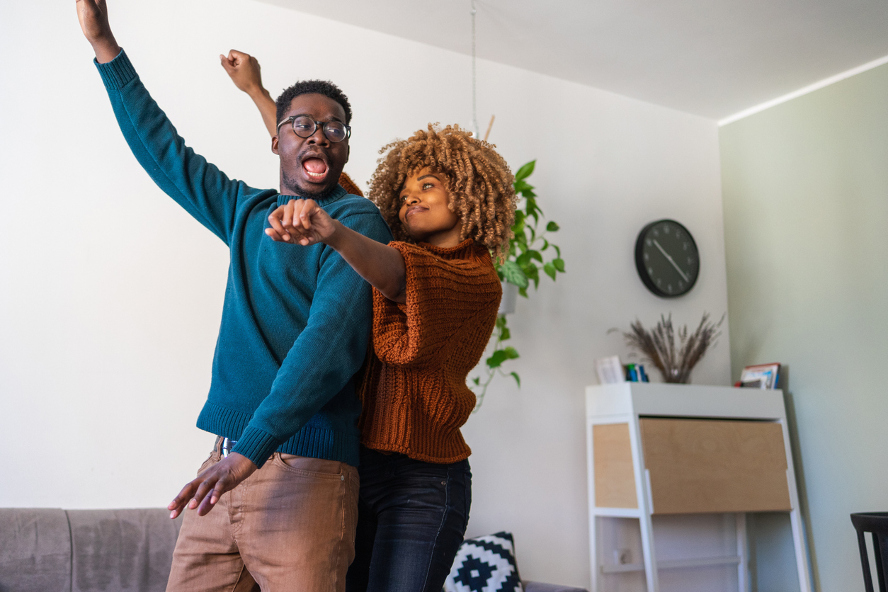 A young African-American couple dances around the house. They look happy in love celebrating their achievements.