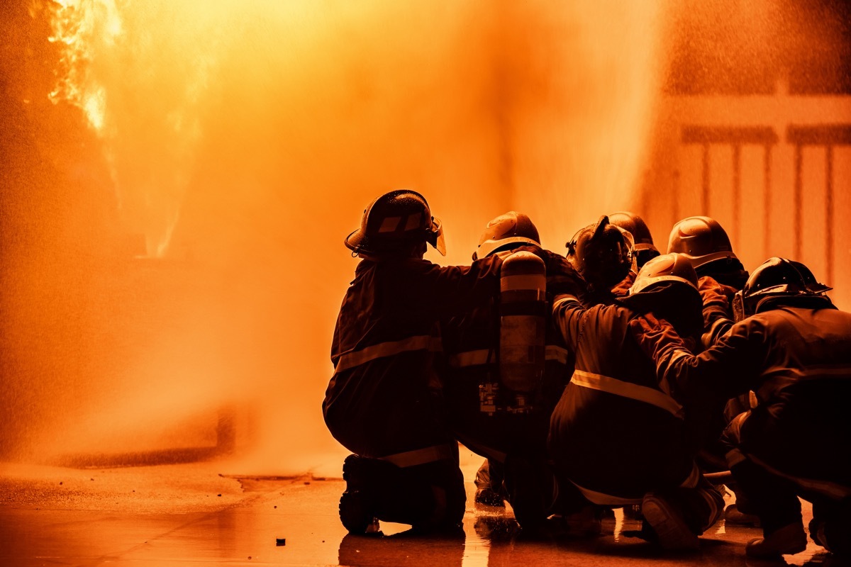 Firefighter using extinguisher or Twirl water fog type fire extinguisher to spray water from hose for fire fighting with fire flame on fuel and control fire for safety in plant of industrial area.