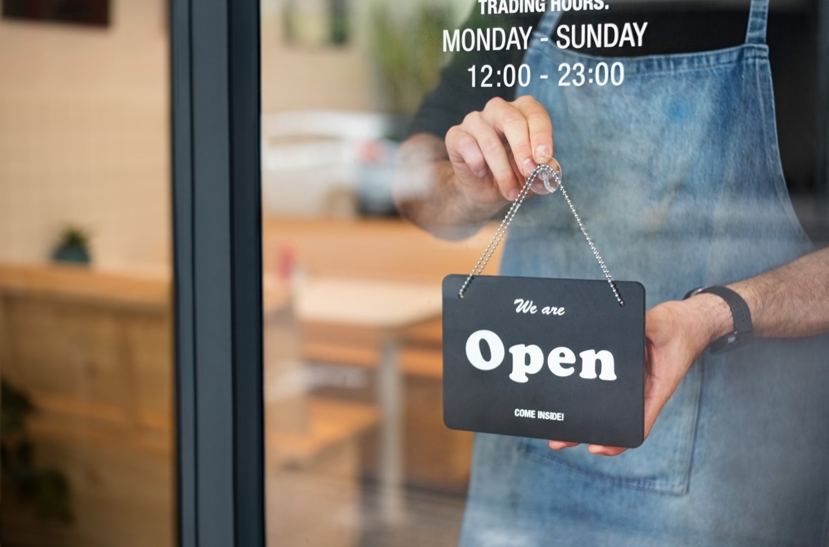 Cropped shot of a man in apron putting nameplate on the entrance door at his own shop