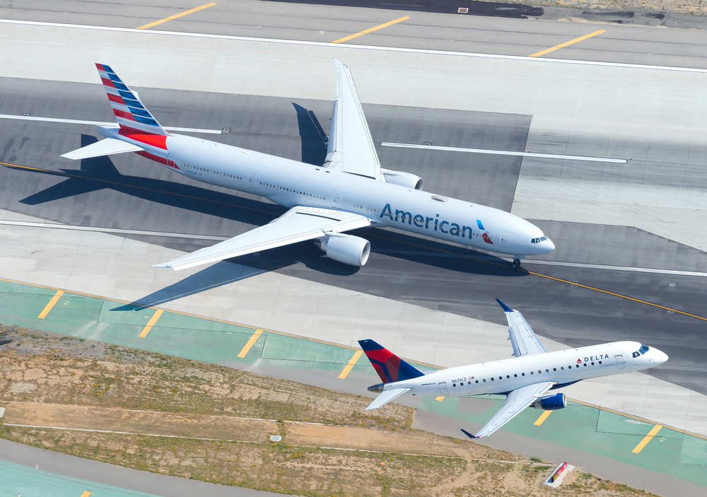 An American Airlines jet taxiing on the runway while a Delta Air Lines jet takes off