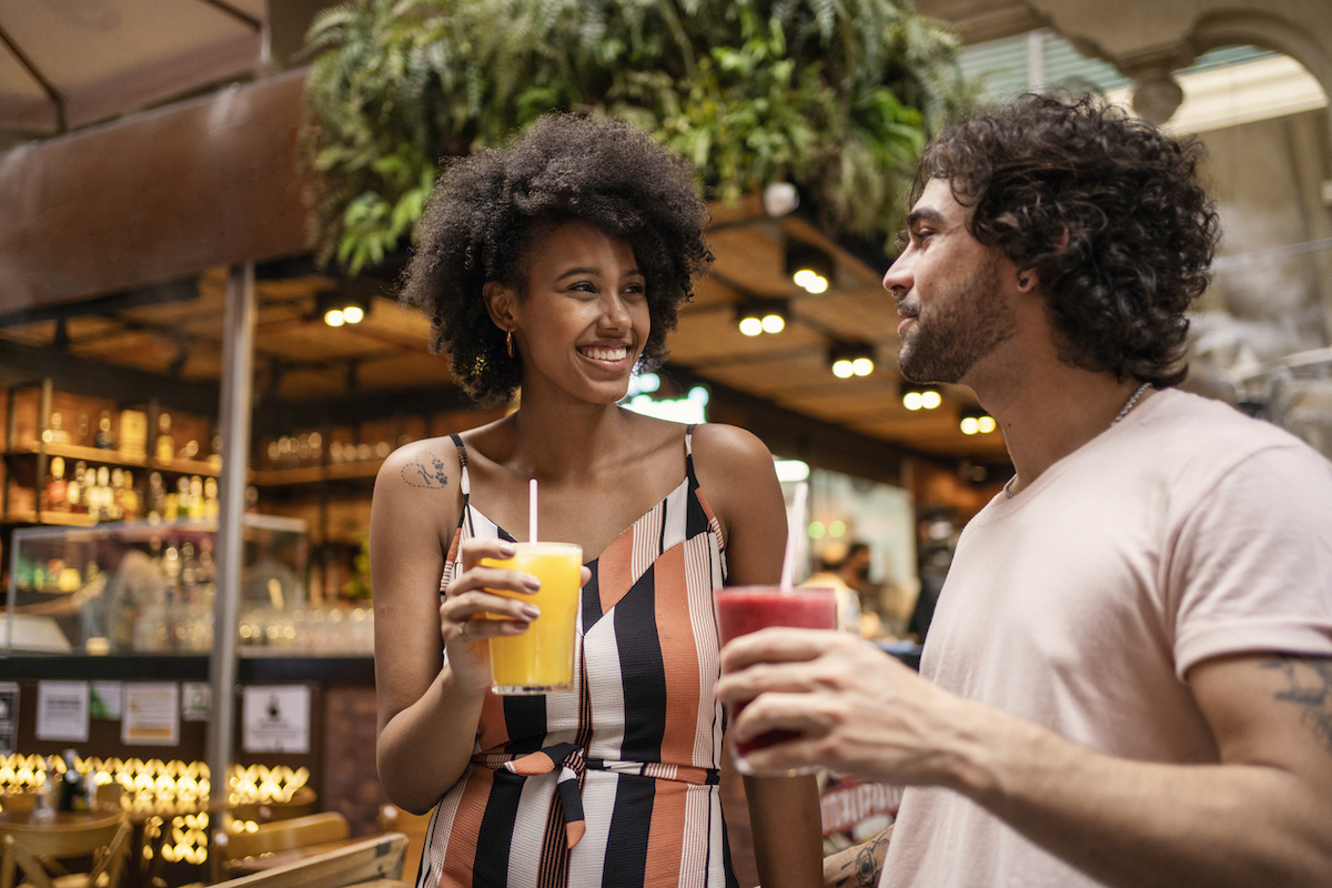 Young couple drinking juice in a market, looking lovingly at each other