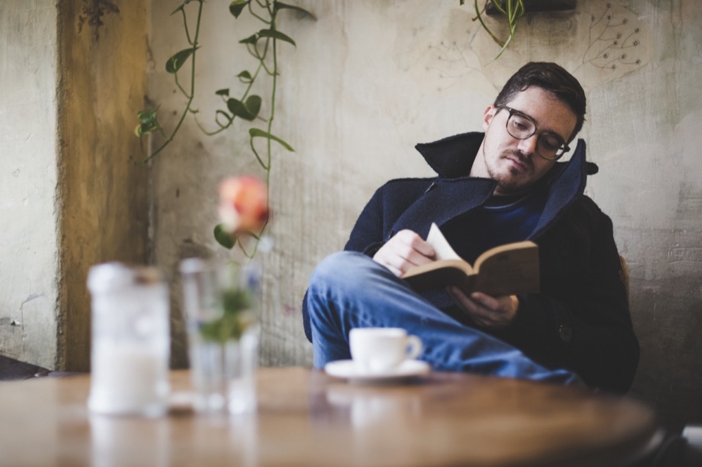 Man with glasses reading a book at a restaurant table, open marriage