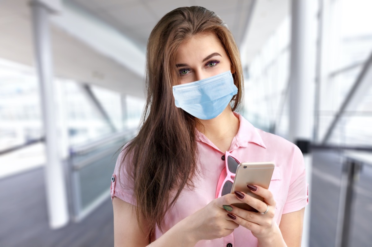 woman in a protective face mask with a smart phone at the public place