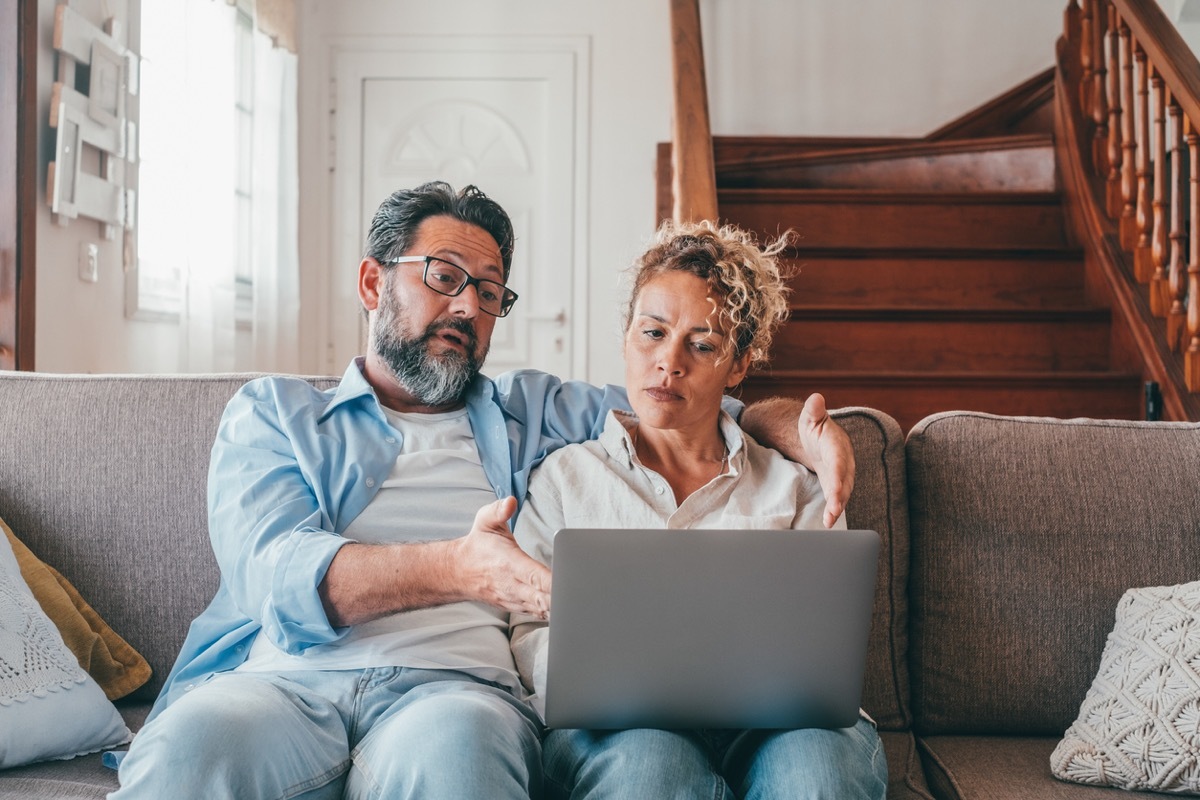 Shocked couple looking at laptop screen frustrated by unexpected bad news online. Husband and wife disappointed and feeling anxious on losing money in online lottery,