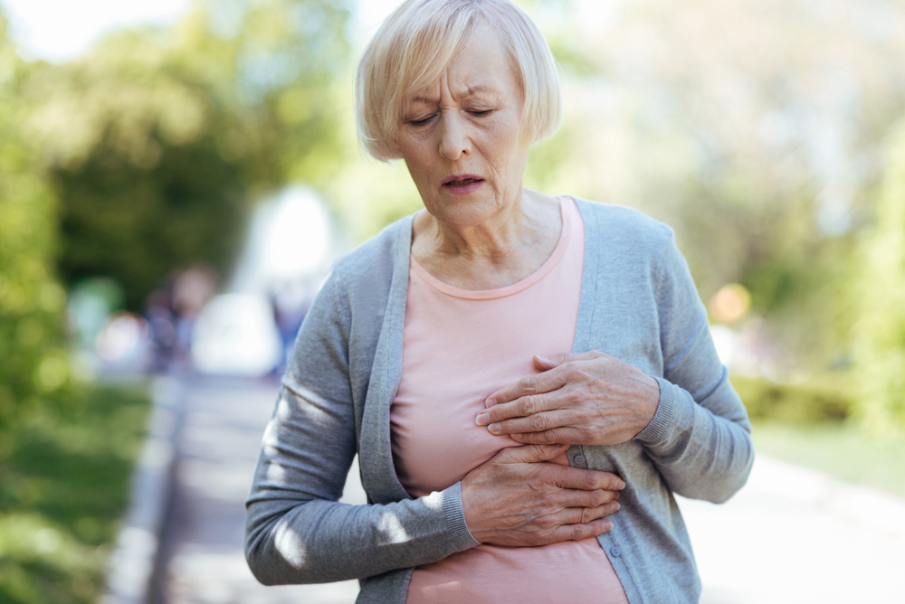 A senior woman walking and holding her chest with heart attack symptoms