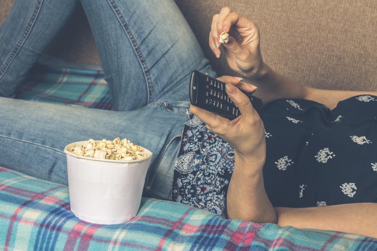 woman eating popcorn laying on the couch watching TV