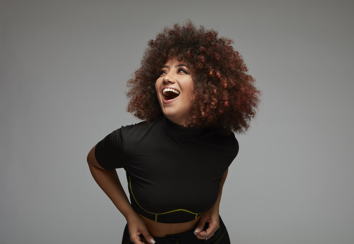 Laughing curly-haired young woman wearing black clothes against gray background