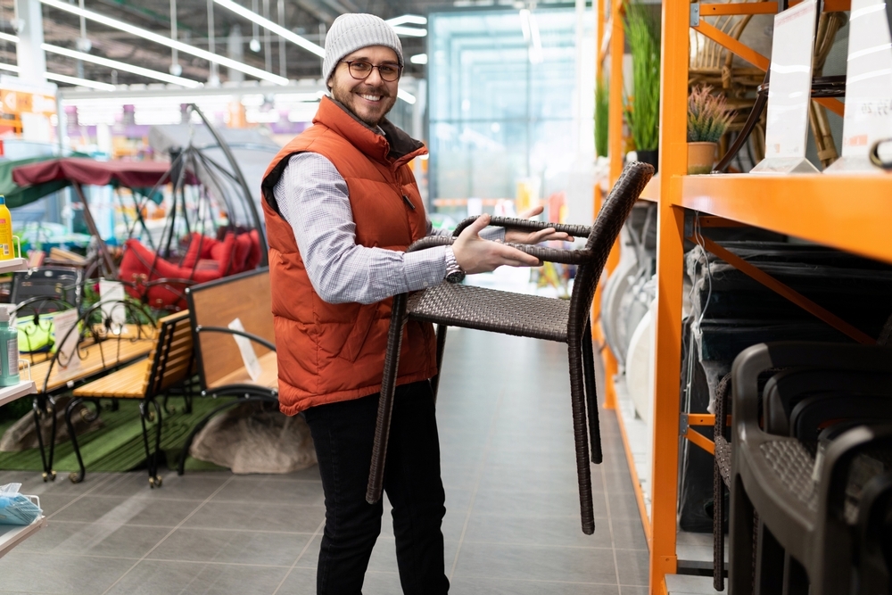 A man holding a patio chair while shopping in a furniture store