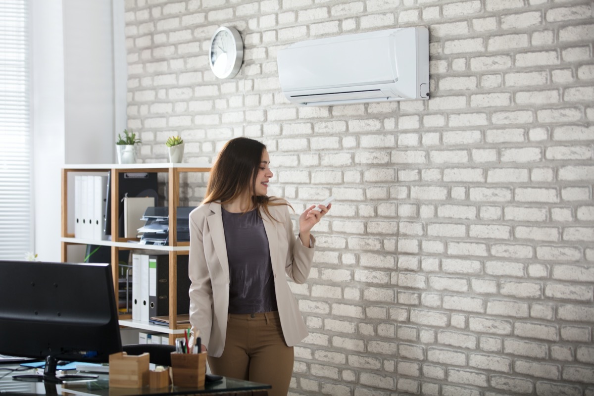 Young Businesswoman Standing In Office Using Remote Control Of Air Conditioner