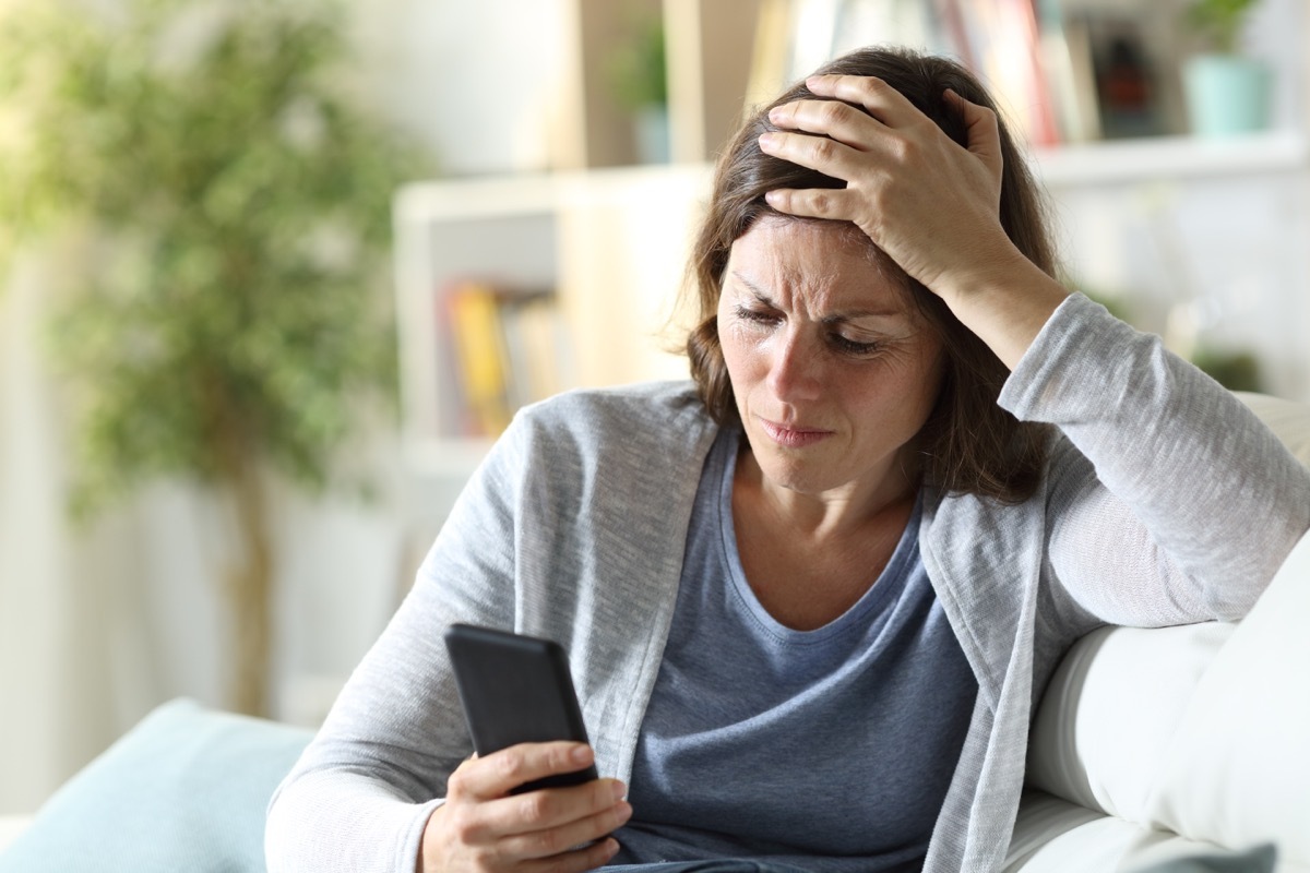 Sad adult woman reading news on phone at home