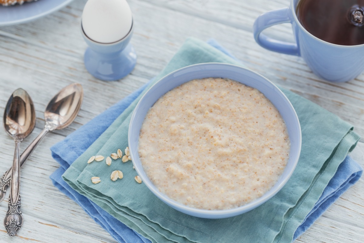 bowl of porridge with black tea and boiled egg on the white wooden background