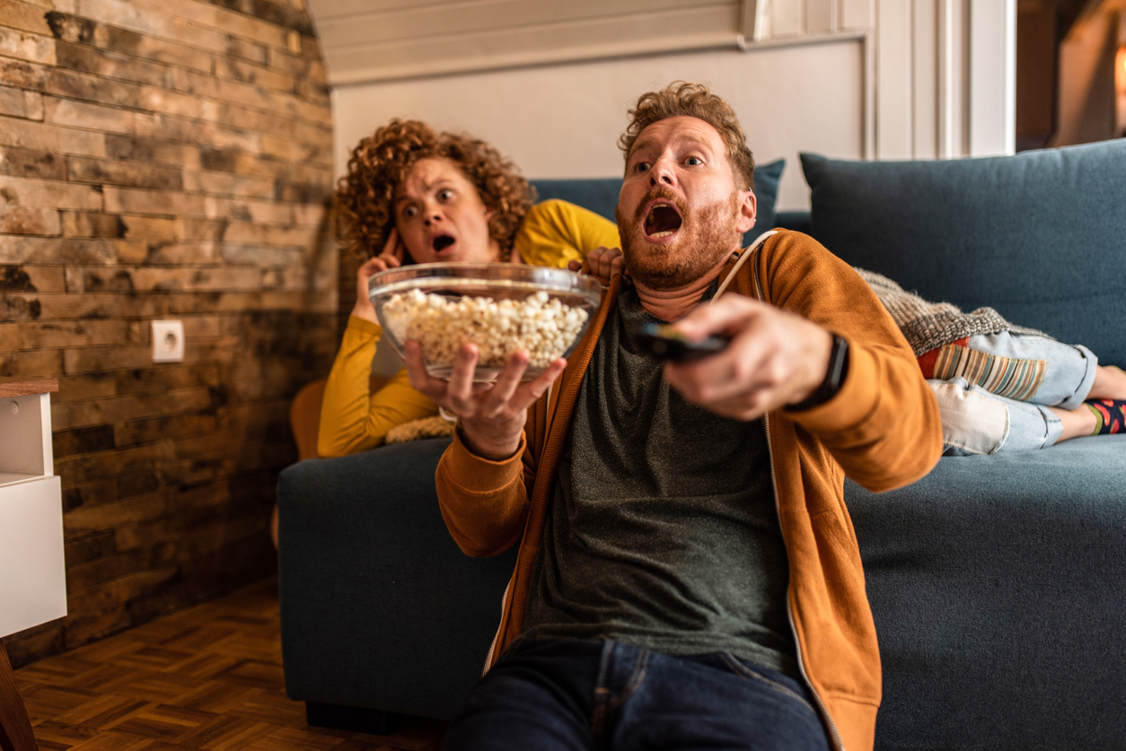 Shocked young ginger couple watching an event on tv.