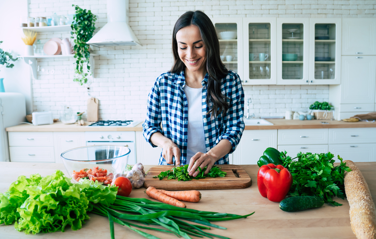 A young woman chopping vegetables on her kitchen island.