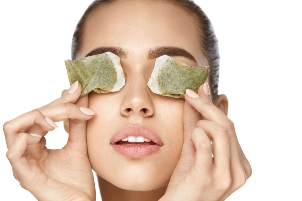 a woman putting chilled green tea bags on her eyes