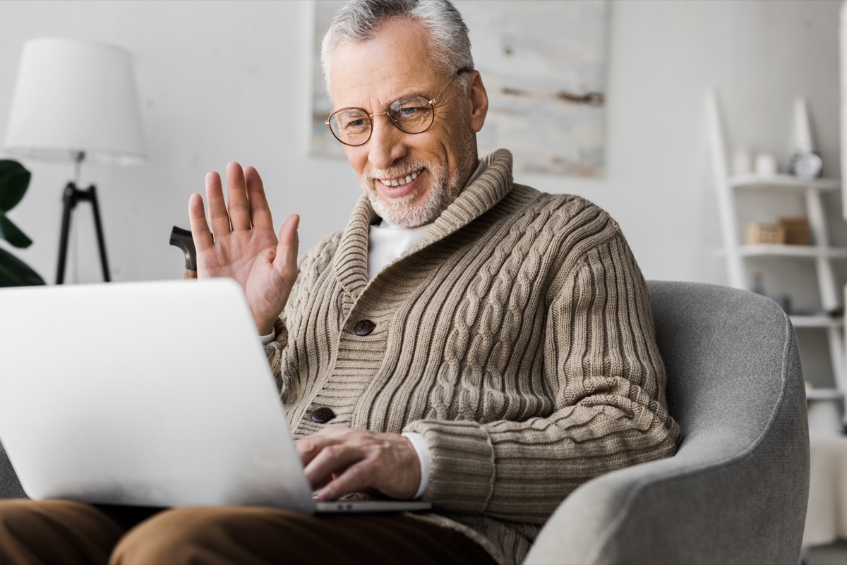 cheerful senior man in glasses waving hand while having video call