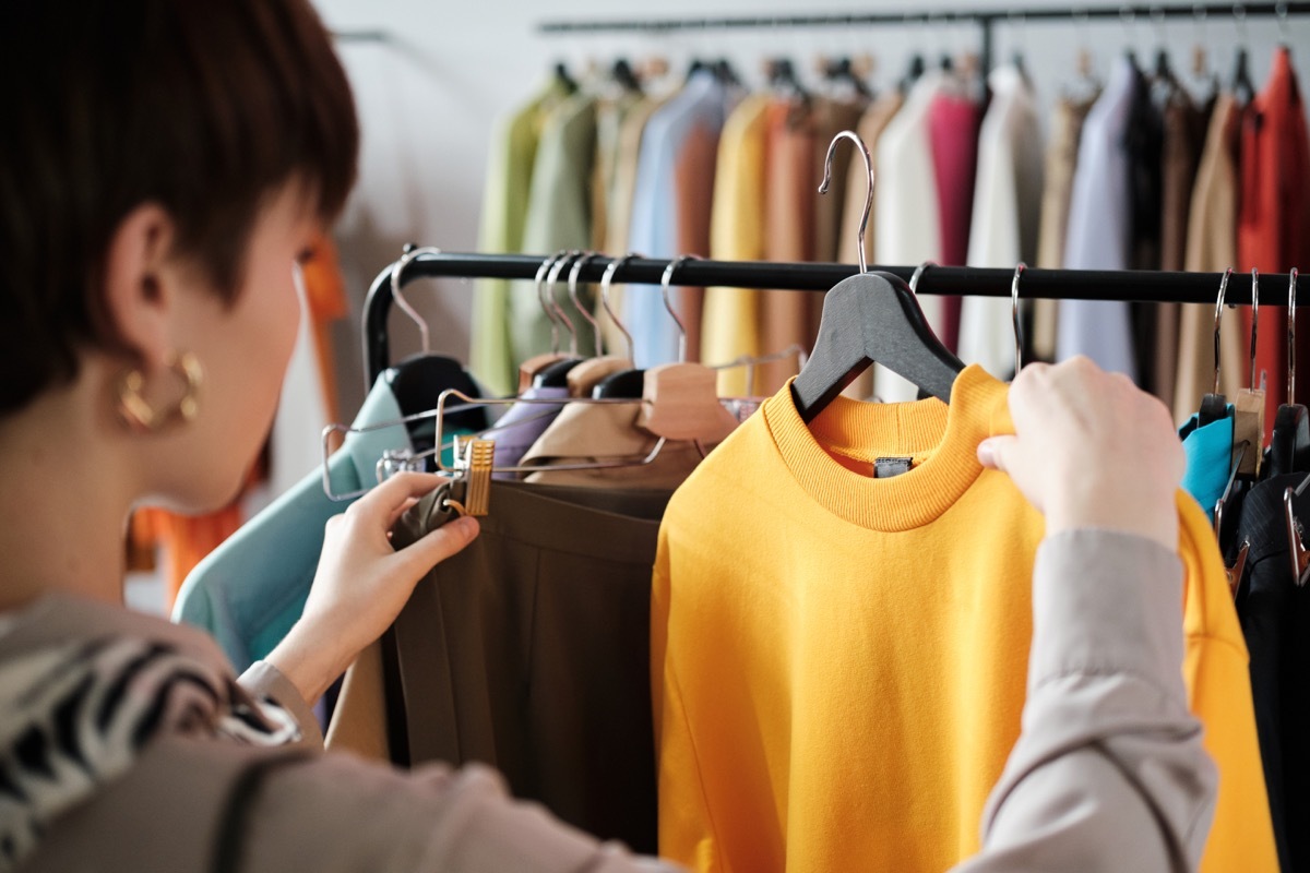 Rear view of young woman looking at clothes on rack in her hands and choosing a new style for herself in the clothes store