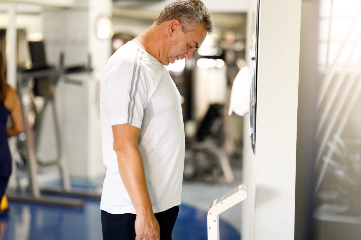 Man weighing himself on a scale at the gym