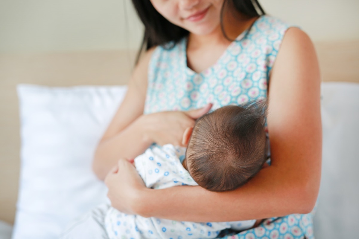 infant baby feeding from mother breastfeeding her newborn child on the bed