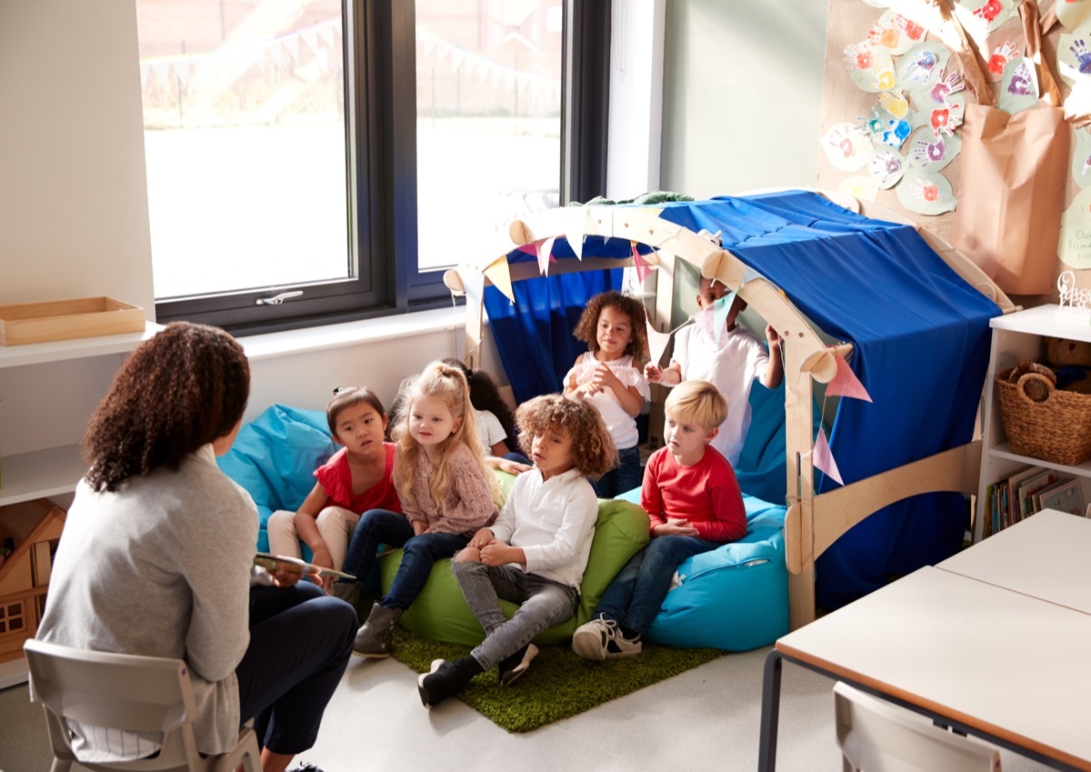 young children in preschool reading nook having a story read to them by their teacher