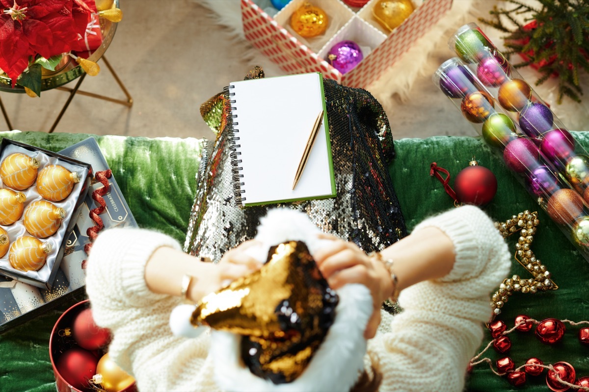 Holiday season. Upper view of stressed stylish housewife in sparkle gold sequin santa hat sitting on sofa in the modern living room at Christmas tired of the holiday bustle.