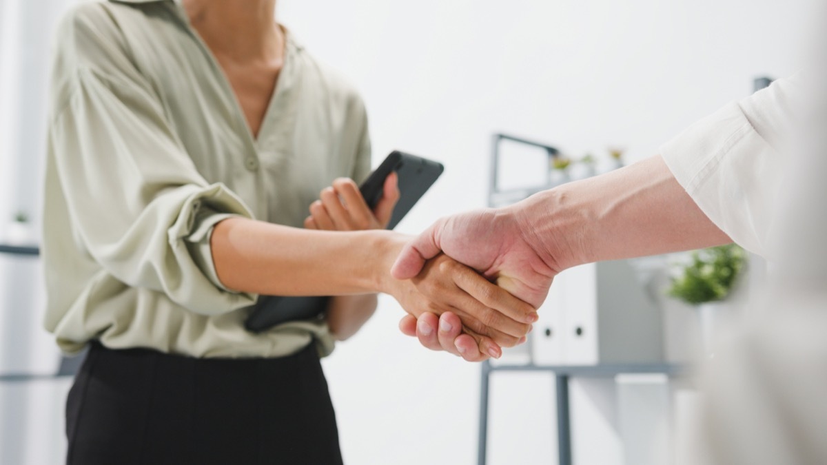 group of young creative people in smart casual wear discussing business shaking hands together and smiling while standing in modern office. Partner cooperation, coworker teamwork concept.