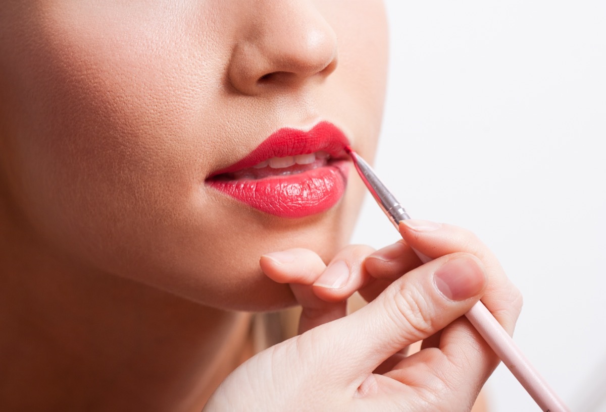 Makeup artist working on a young blonde woman applying a lip stain