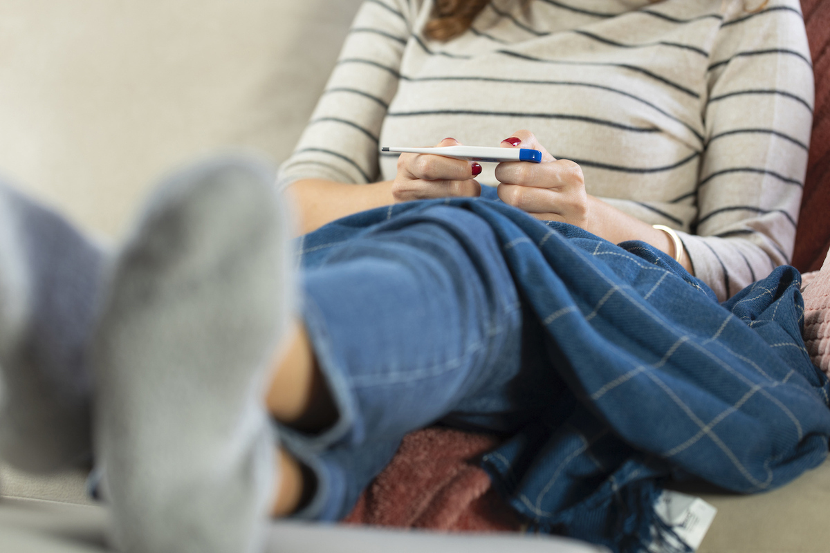 young woman sitting on couch looking at thermometer 