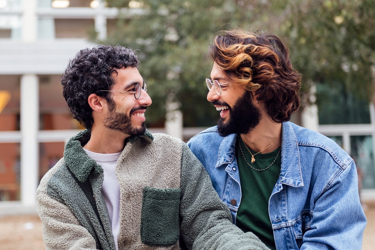 couple of men sitting in a park laughing happy,