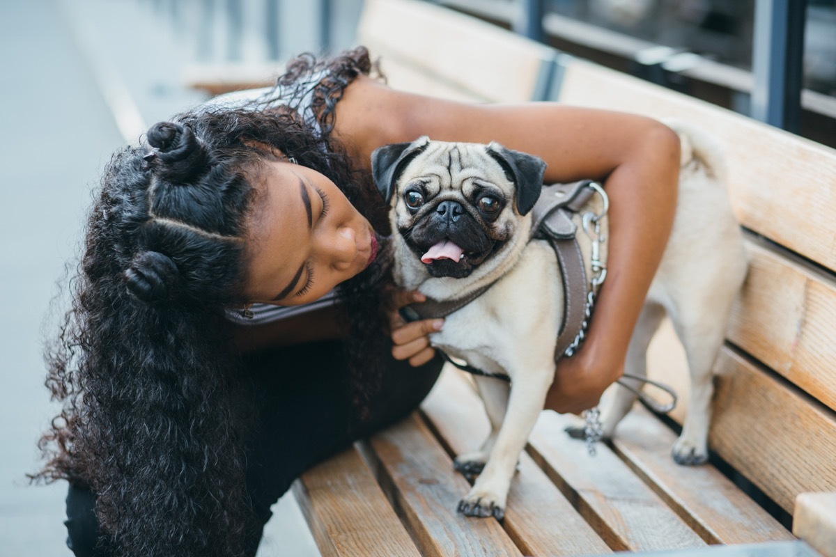 girl hugging her pug on a park nech