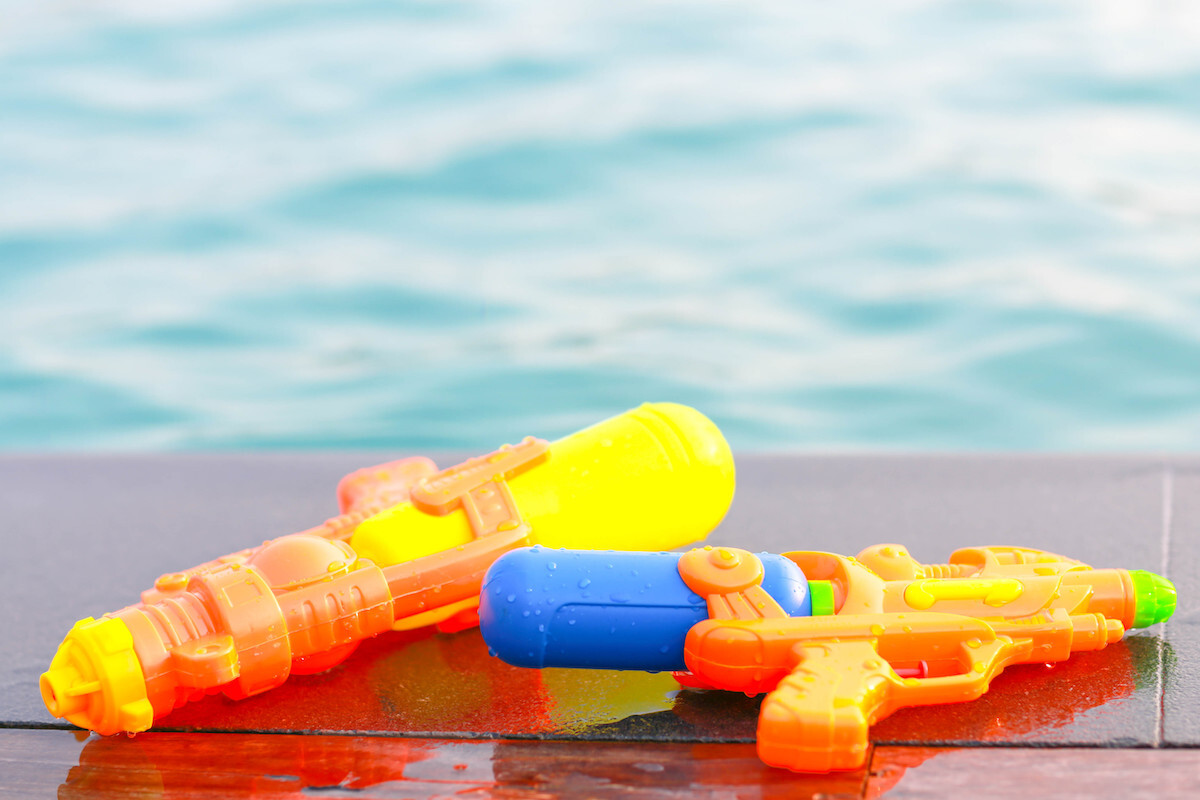 Two orange water guns up close with a pool in the background