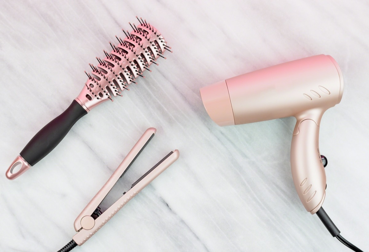 hair dryer, brush, straightener on a marble countertop