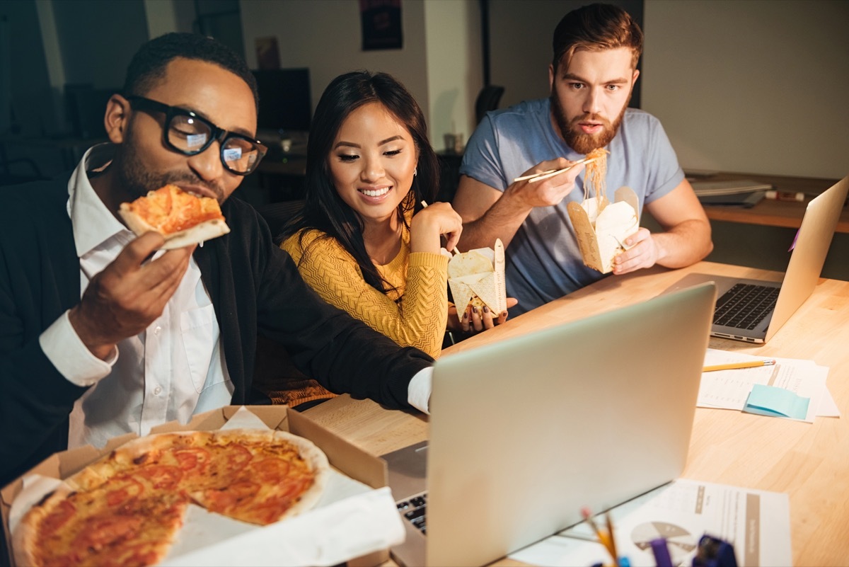 Three young coworkers eat pizza late at night, high cholesterol