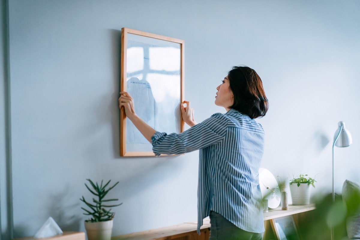 Young woman decorating and putting up a picture frame on the wall at home