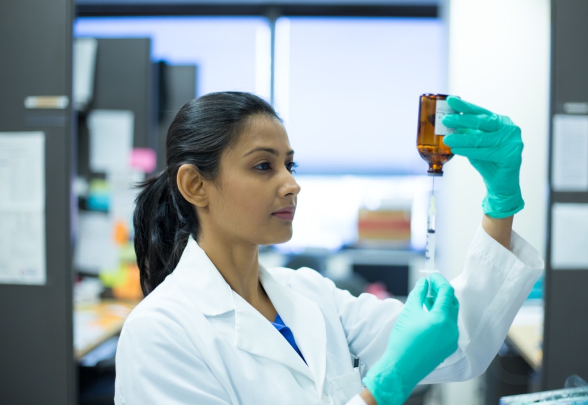 woman scientist in white labcoat holding syringe needle and brown bottle