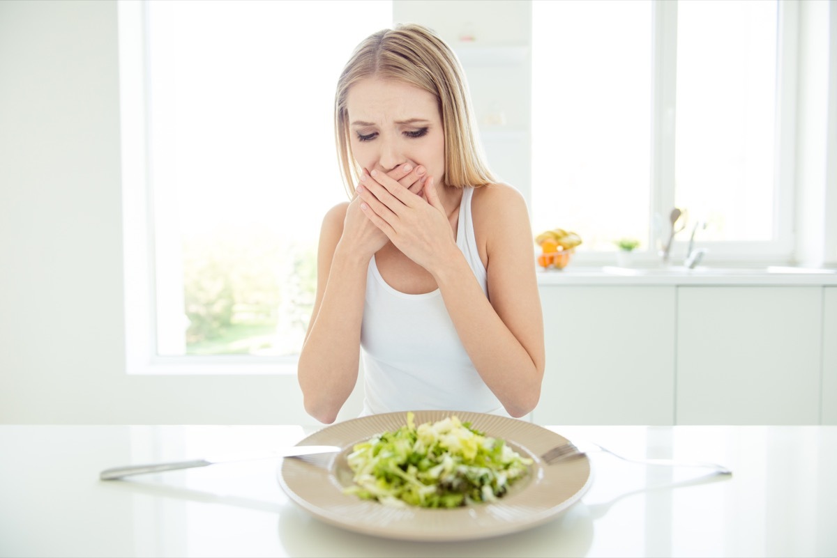 frustrated confused tired scared displeased lady covering mouth with palms do not want to eat salad sitting at table looking at bowl